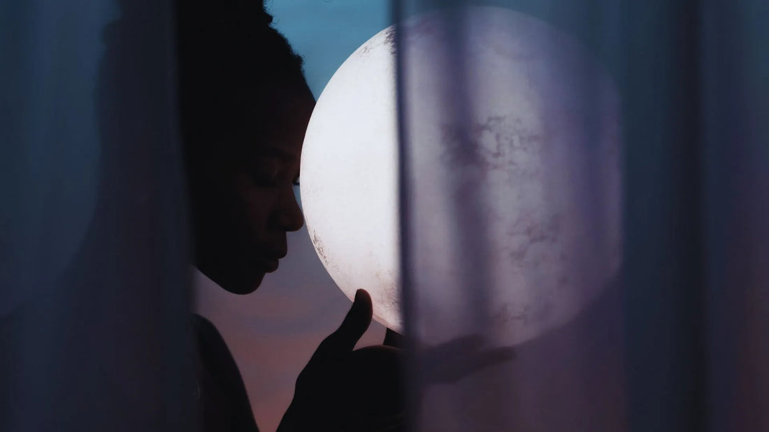 Femme tenant la pleine lune contre son front, ambiance calme et méditative.