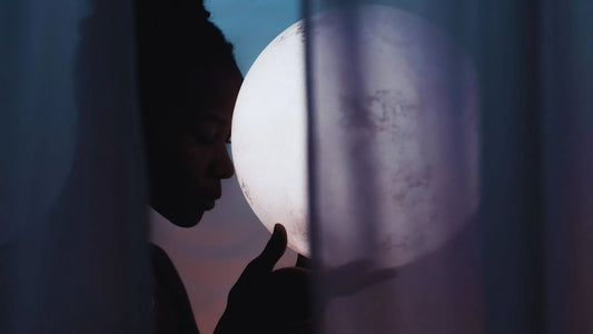 Femme tenant la pleine lune contre son front, ambiance calme et méditative.