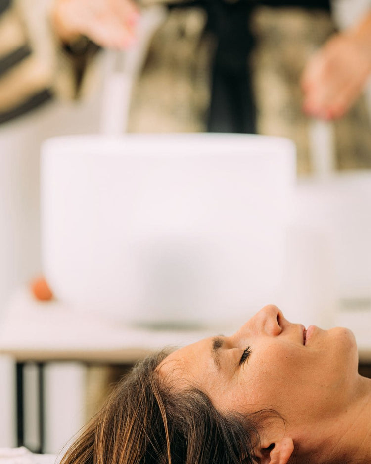 Utiliser un bol chantant sonore pendant une prestation avec une femme qui ferme les yeux pour ressentir les fréquences vibratoires